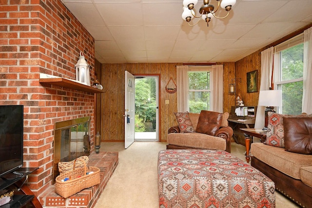 carpeted living room with a paneled ceiling, a notable chandelier, a brick fireplace, and wood walls