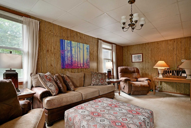 carpeted living room with wood walls, an inviting chandelier, and a paneled ceiling