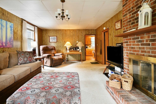 living room featuring brick wall, light carpet, wood walls, a brick fireplace, and an inviting chandelier