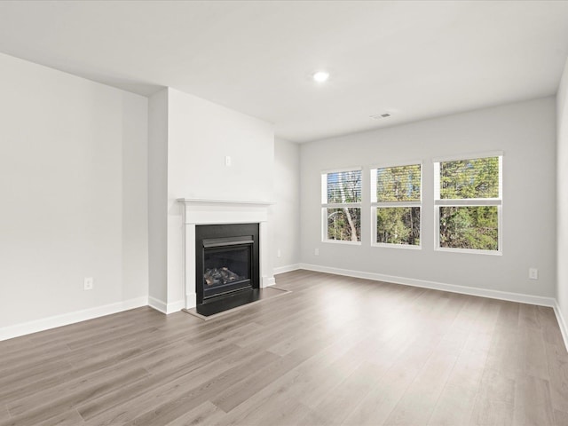 unfurnished living room featuring recessed lighting, visible vents, a glass covered fireplace, wood finished floors, and baseboards