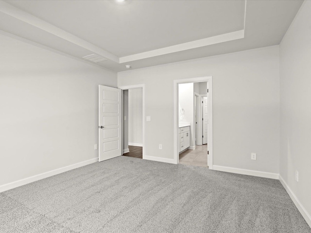 unfurnished bedroom with carpet floors, a tray ceiling, ensuite bath, and baseboards