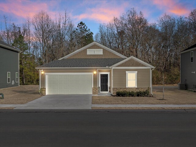 craftsman-style home with roof with shingles, central air condition unit, an attached garage, stone siding, and driveway