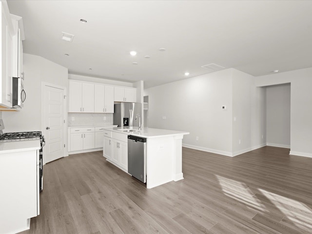 kitchen featuring stainless steel appliances, light countertops, light wood-style flooring, an island with sink, and baseboards