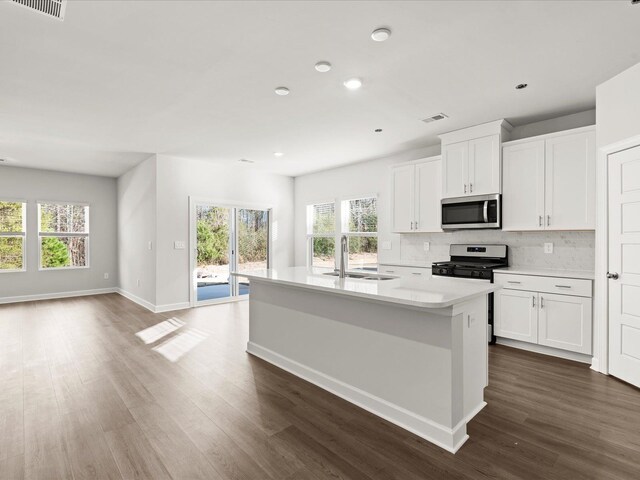 kitchen featuring stainless steel appliances, a sink, visible vents, backsplash, and a center island with sink