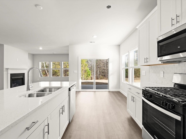 kitchen featuring decorative backsplash, a glass covered fireplace, stainless steel appliances, light wood-style floors, and a sink