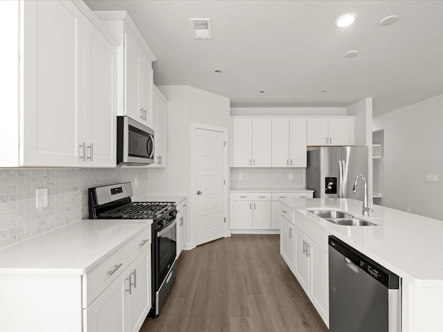 kitchen featuring stainless steel appliances, dark wood-style flooring, a sink, visible vents, and an island with sink