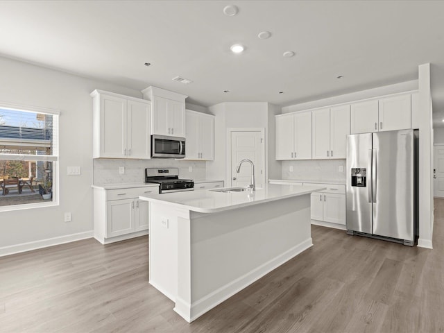 kitchen featuring stainless steel appliances, light countertops, a center island with sink, and white cabinets