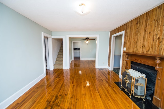 unfurnished living room featuring ceiling fan, wood-type flooring, and wooden walls