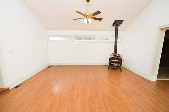 empty room featuring ceiling fan, light wood-type flooring, and a wood stove