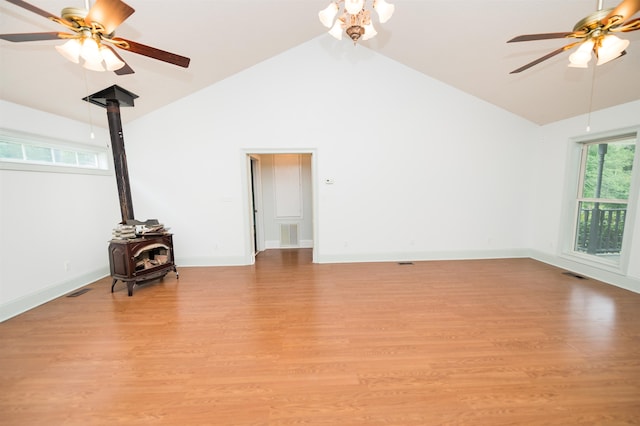 empty room featuring ceiling fan, high vaulted ceiling, light hardwood / wood-style floors, and a wood stove