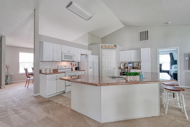 kitchen with white appliances, a center island with sink, white cabinetry, and light colored carpet