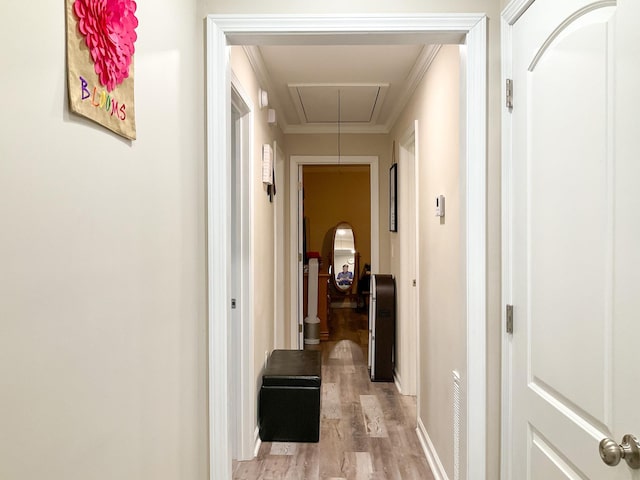 hall with attic access, baseboards, ornamental molding, and light wood finished floors