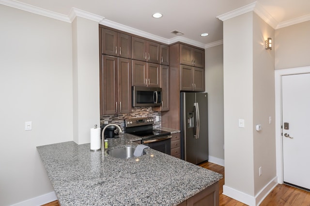 kitchen with light wood-type flooring, kitchen peninsula, appliances with stainless steel finishes, and backsplash