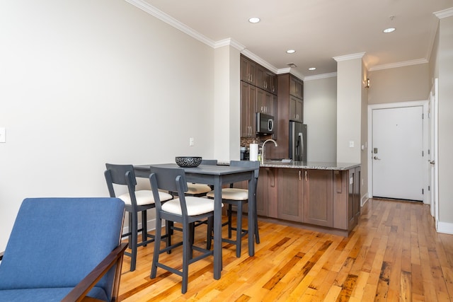 kitchen featuring stainless steel appliances, ornamental molding, light wood-type flooring, and light stone counters