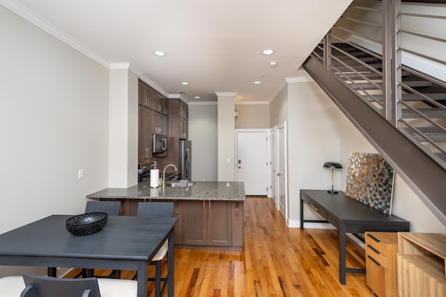 kitchen featuring stainless steel appliances, light hardwood / wood-style floors, dark brown cabinetry, crown molding, and dark stone countertops