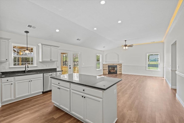 kitchen featuring a stone fireplace, visible vents, ceiling fan, dishwasher, and a sink