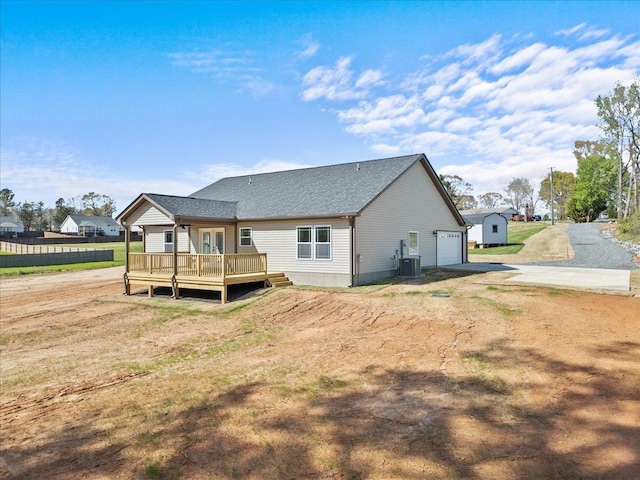 back of property featuring central AC, a shingled roof, a garage, a wooden deck, and driveway