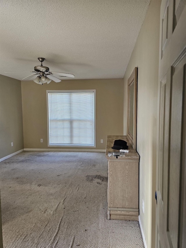 interior space with light carpet, ceiling fan, baseboards, and a textured ceiling