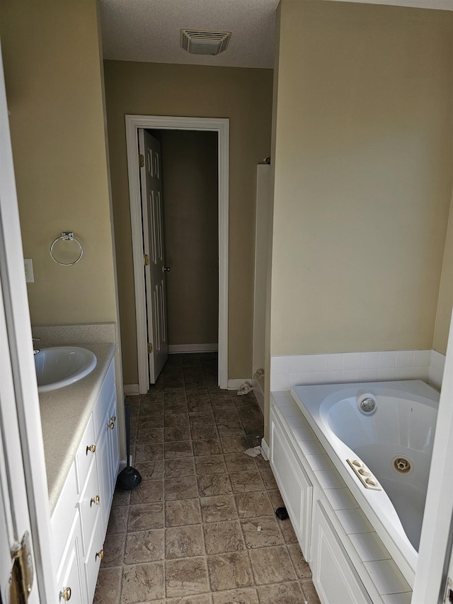 full bath with visible vents, vanity, a textured ceiling, a jetted tub, and baseboards