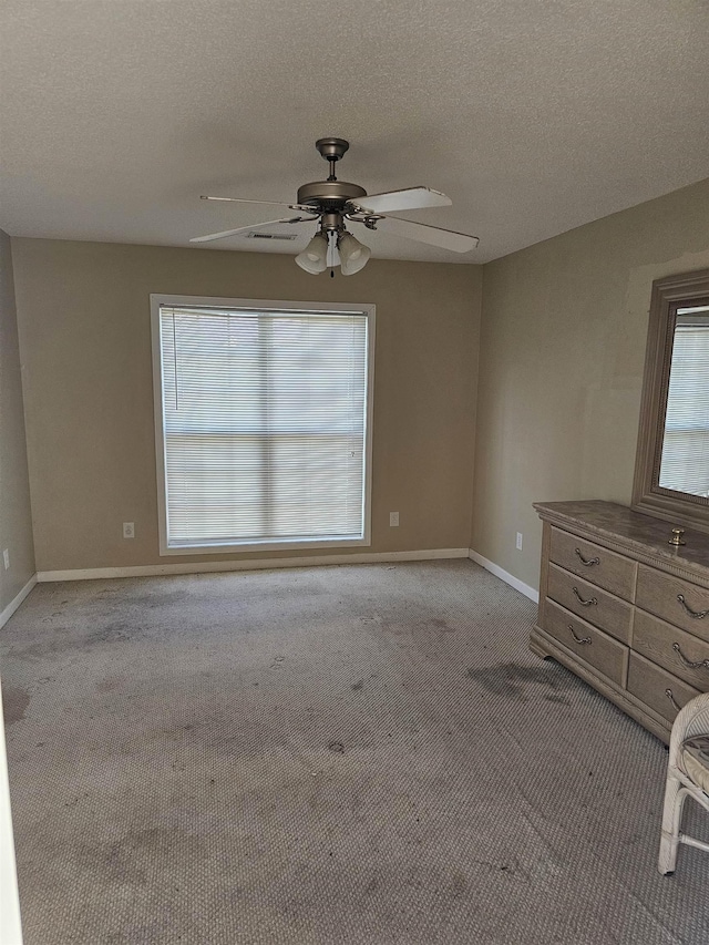 unfurnished bedroom featuring carpet floors, visible vents, a ceiling fan, a textured ceiling, and baseboards