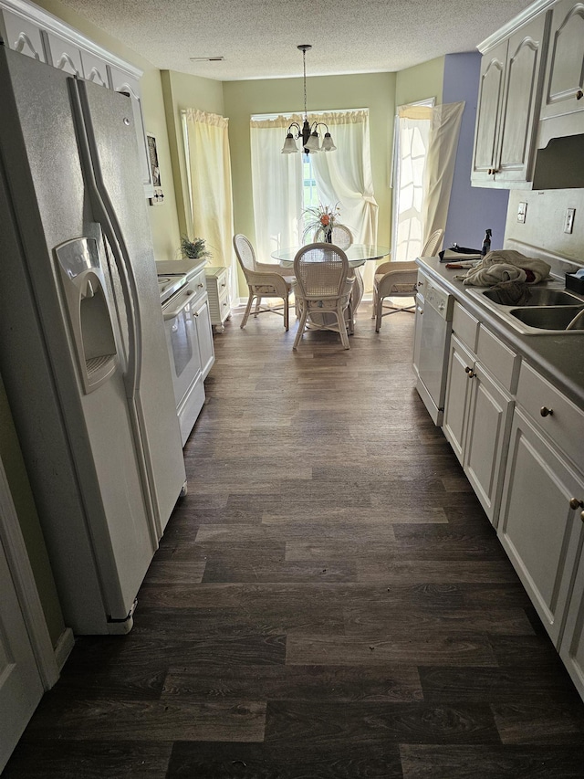 kitchen featuring dark wood-style floors, hanging light fixtures, a sink, a textured ceiling, and white appliances