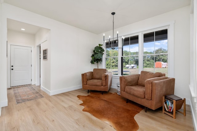 living area with light wood-style floors, baseboards, and an inviting chandelier