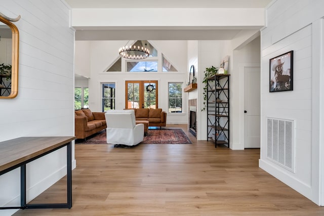 living area featuring a fireplace, visible vents, french doors, light wood-type flooring, and an inviting chandelier