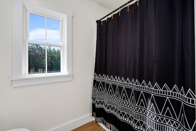 full bath with a shower with shower curtain, wood finished floors, and baseboards