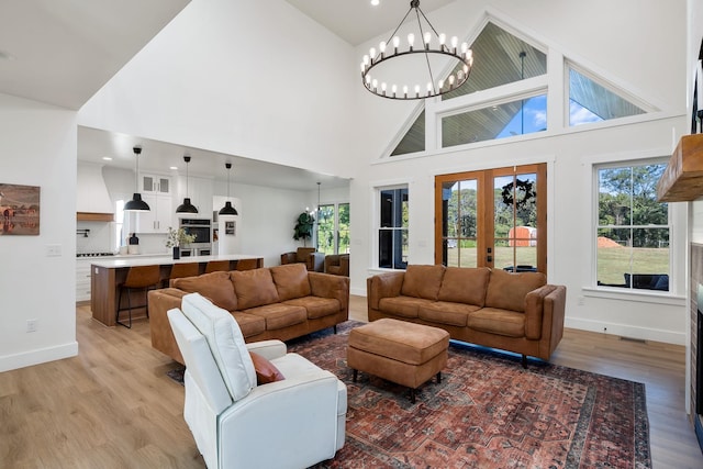 living area featuring baseboards, high vaulted ceiling, light wood-style floors, and a notable chandelier