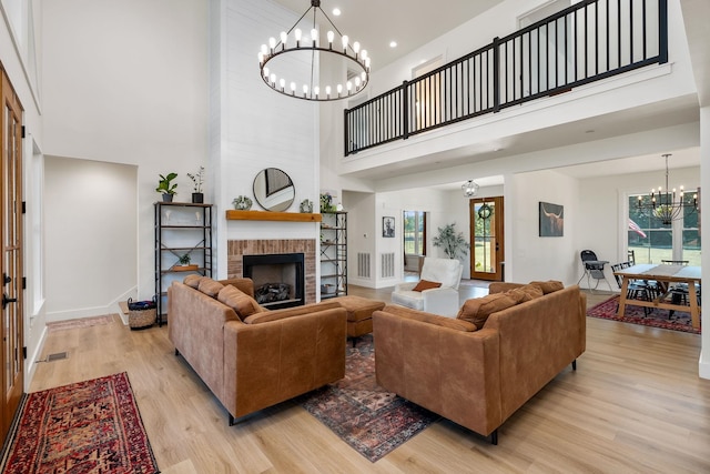 living room featuring light wood finished floors, baseboards, a towering ceiling, a fireplace, and a notable chandelier