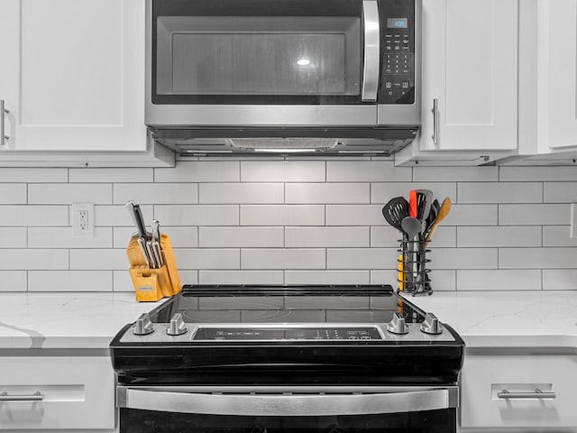 kitchen featuring light stone counters, appliances with stainless steel finishes, white cabinets, and decorative backsplash