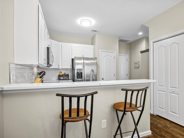 kitchen featuring a breakfast bar area, dark hardwood / wood-style flooring, tasteful backsplash, stainless steel appliances, and kitchen peninsula