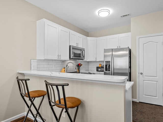 kitchen with appliances with stainless steel finishes, a kitchen bar, kitchen peninsula, decorative backsplash, and white cabinetry