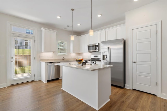 kitchen featuring hardwood / wood-style floors, appliances with stainless steel finishes, a kitchen island, and white cabinetry