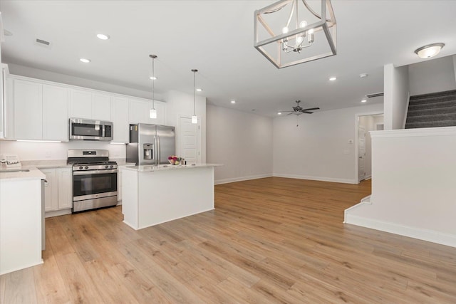 kitchen with ceiling fan with notable chandelier, decorative light fixtures, a kitchen island, appliances with stainless steel finishes, and light hardwood / wood-style floors