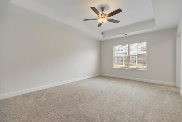 carpeted empty room with a raised ceiling and ceiling fan