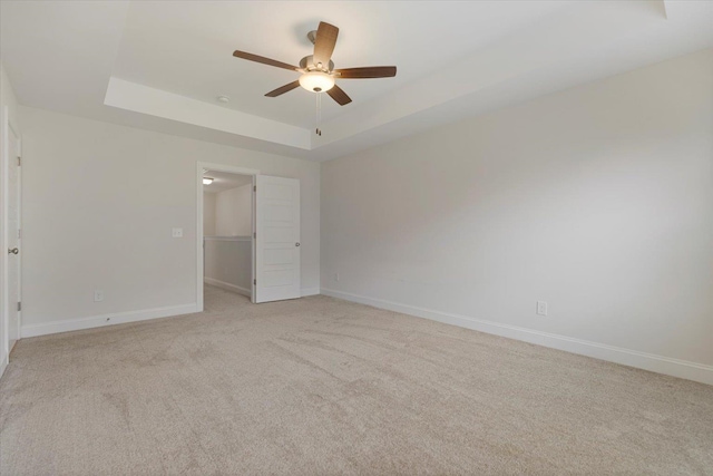 unfurnished bedroom with light carpet, a tray ceiling, a ceiling fan, and baseboards