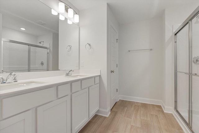 full bath with double vanity, a stall shower, a sink, and wood finished floors