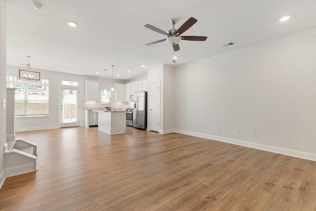 unfurnished living room featuring light wood-style floors, recessed lighting, baseboards, and ceiling fan with notable chandelier