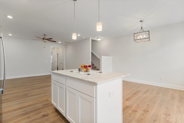 kitchen with white cabinets, ceiling fan with notable chandelier, a center island, and light hardwood / wood-style flooring