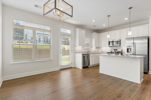 kitchen with a healthy amount of sunlight, stainless steel appliances, hanging light fixtures, and white cabinets