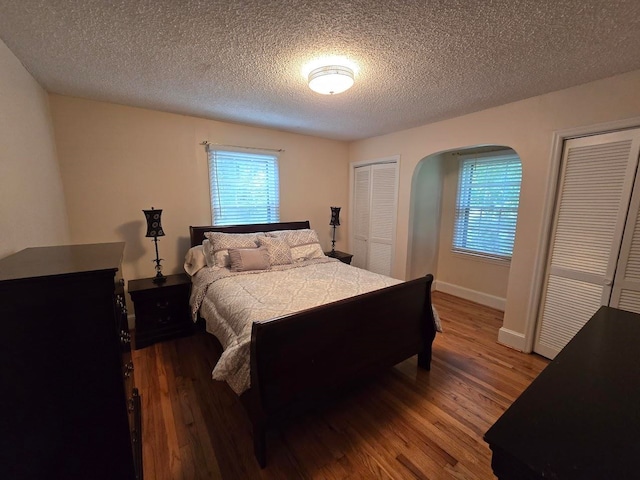 bedroom featuring two closets, dark hardwood / wood-style flooring, and a textured ceiling