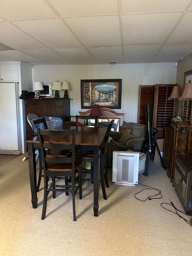 dining space featuring wood walls, carpet flooring, and a drop ceiling