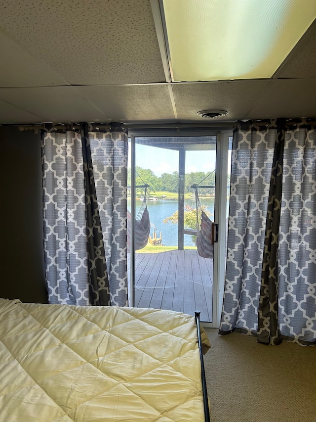 unfurnished bedroom with access to exterior, a water view, a paneled ceiling, and carpet floors