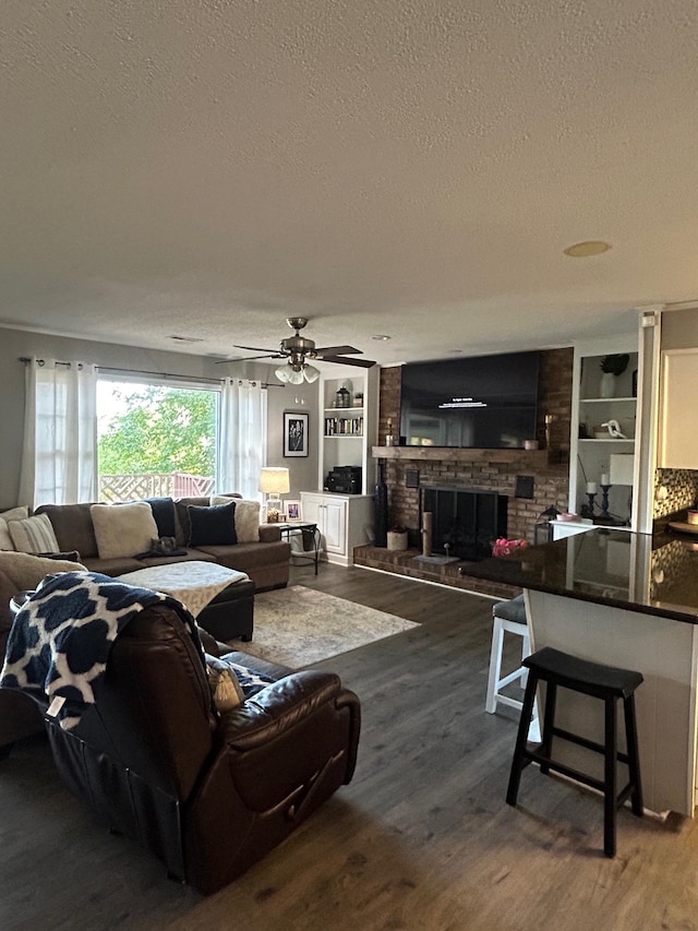 living room featuring built in shelves, a textured ceiling, a brick fireplace, ceiling fan, and hardwood / wood-style flooring