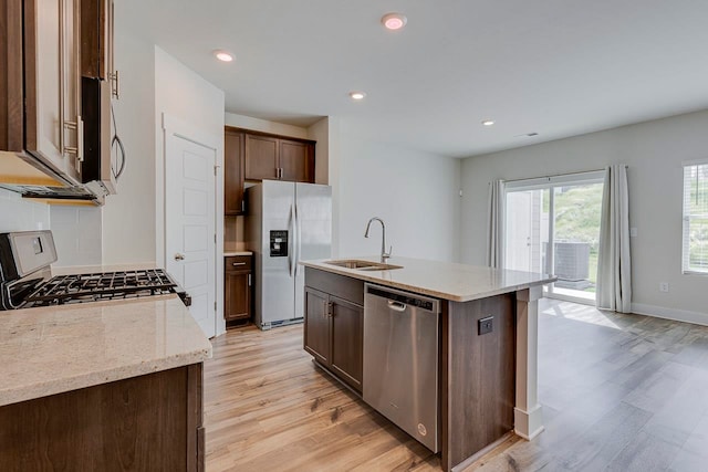 kitchen with light hardwood / wood-style flooring, appliances with stainless steel finishes, an island with sink, sink, and light stone counters