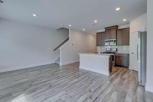 kitchen with a center island with sink, stainless steel appliances, light wood-type flooring, and decorative backsplash