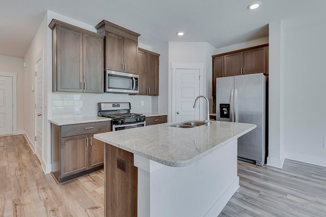 kitchen with appliances with stainless steel finishes, light stone counters, an island with sink, and sink