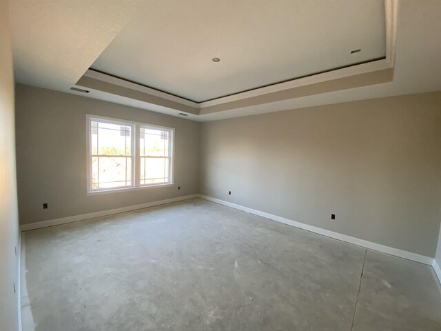 unfurnished room featuring unfinished concrete flooring, a raised ceiling, and baseboards