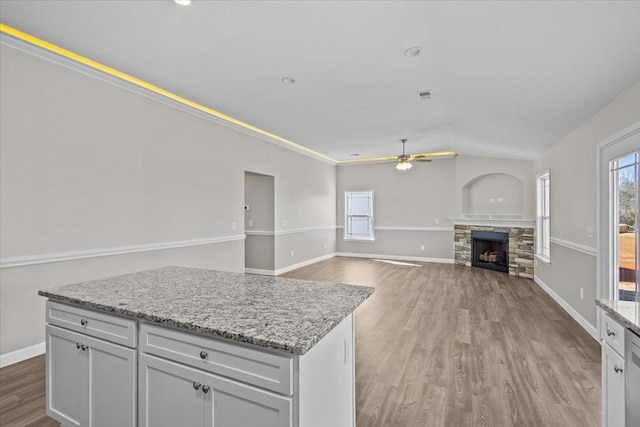 kitchen with plenty of natural light, a ceiling fan, wood finished floors, and a stone fireplace